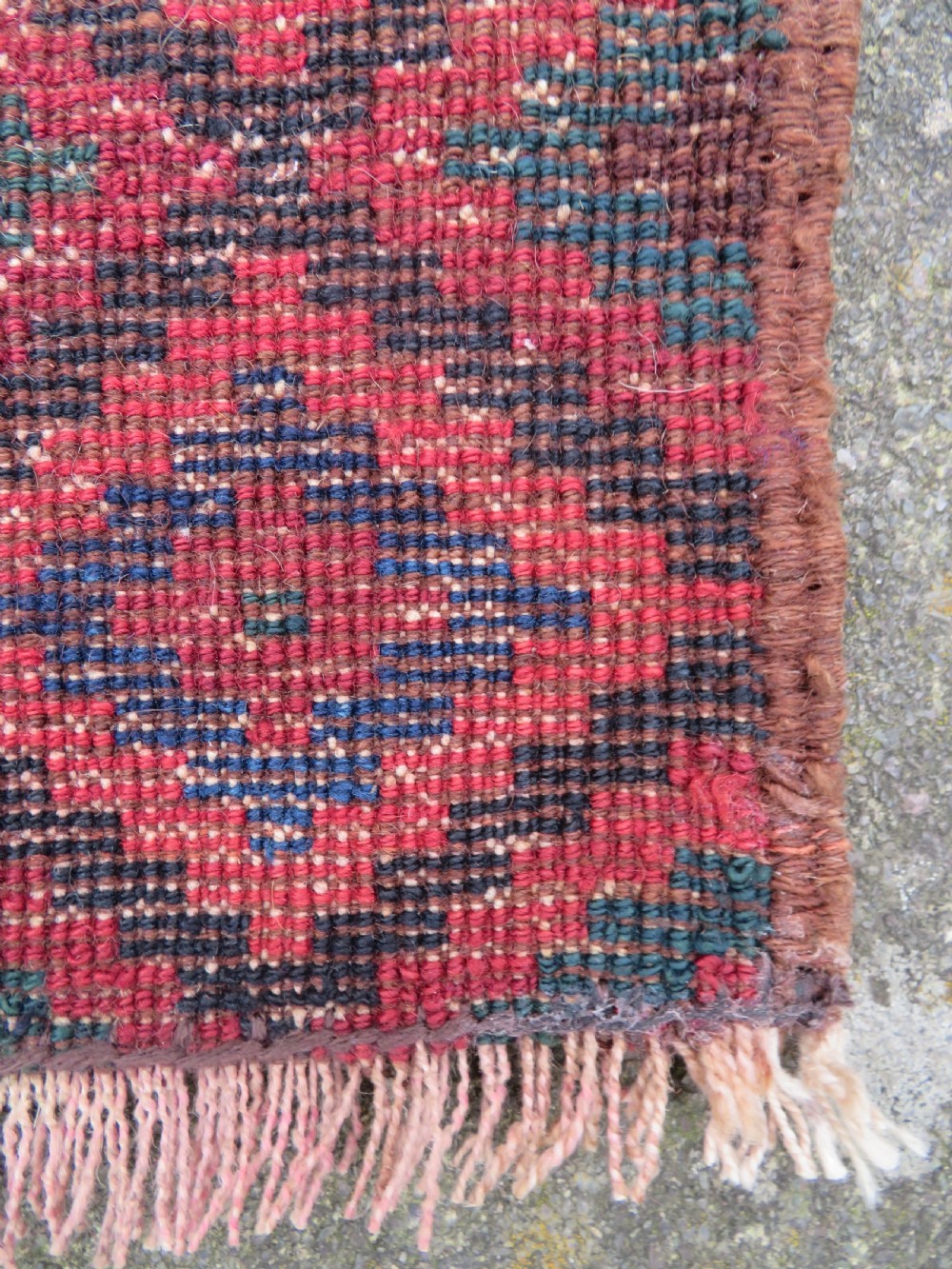 An antique hand-woven Luri saddle bag face featuring a repeating geometric diamond lattice pattern in shades of red, dark blue, cyan, and orange with fringed edges. View V