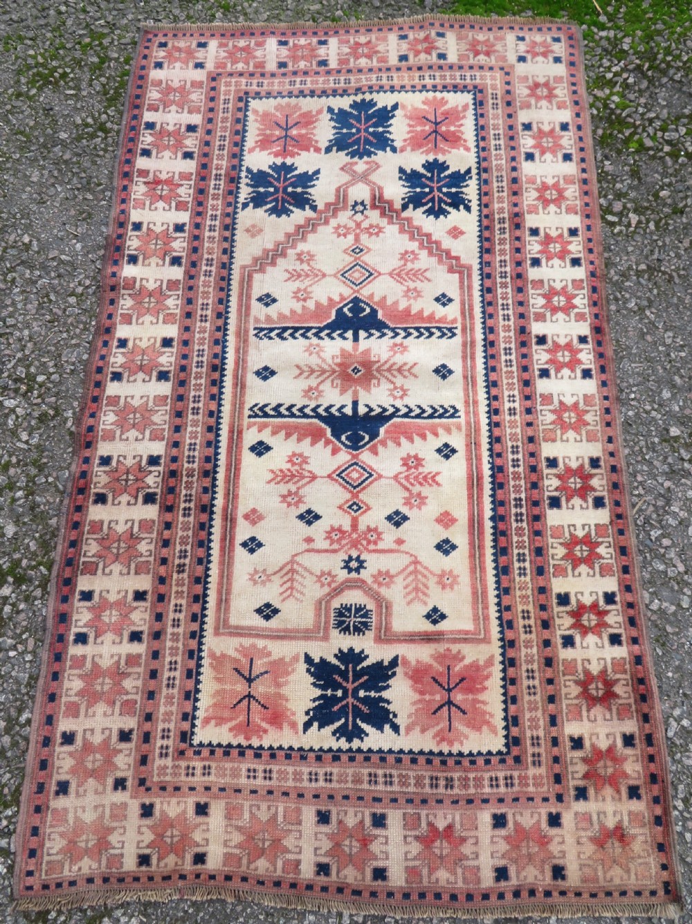 A hand-knotted wool Anatolian Bergama prayer rug featuring an ivory central field with a geometric arched mihrab design framed by terracotta and navy blue geometric borders.