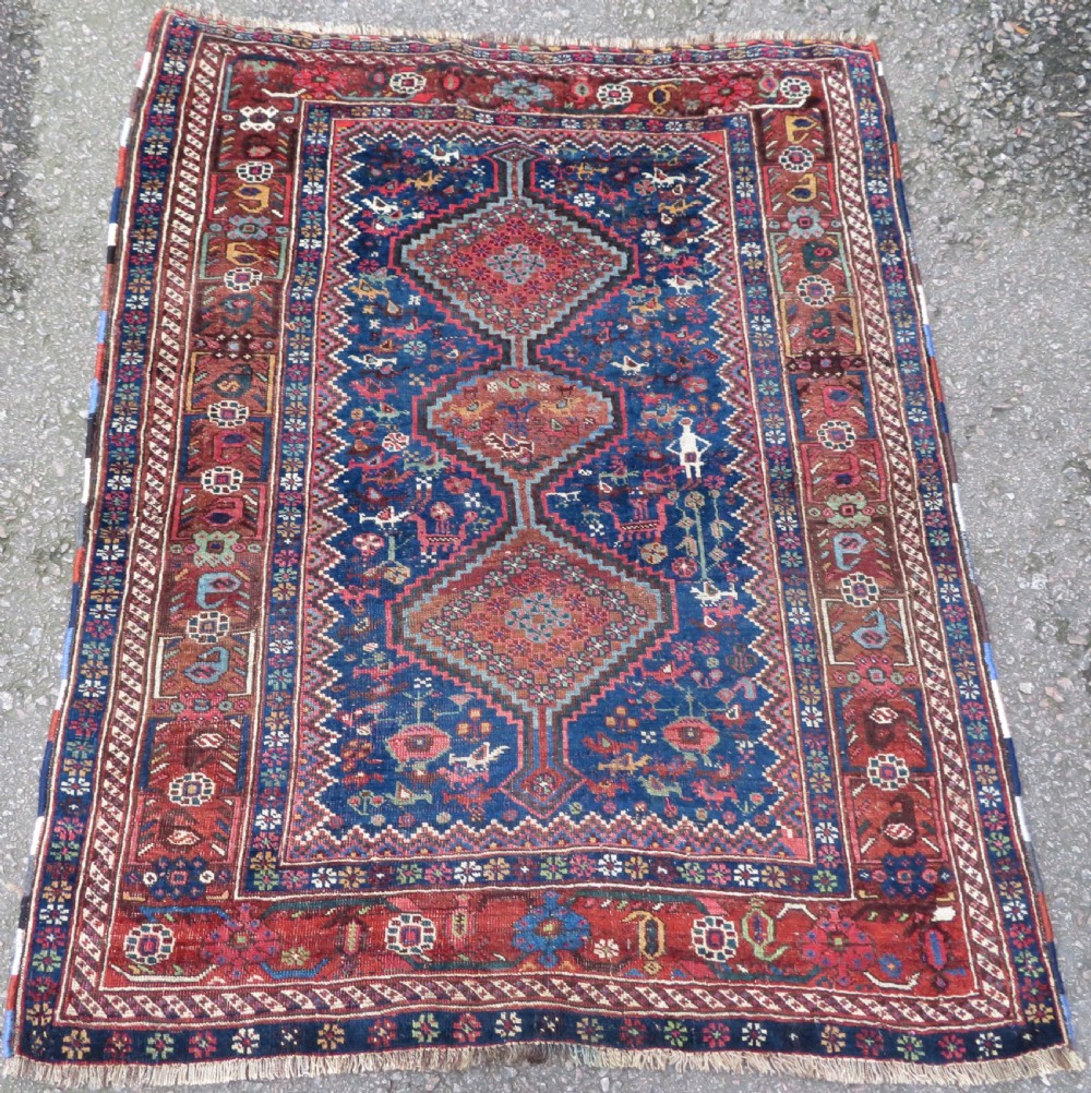 An antique Persian Khamseh rug featuring three central diamond medallions surrounded by small animal motifs and a geometric border in indigo blue and terracotta red tones.