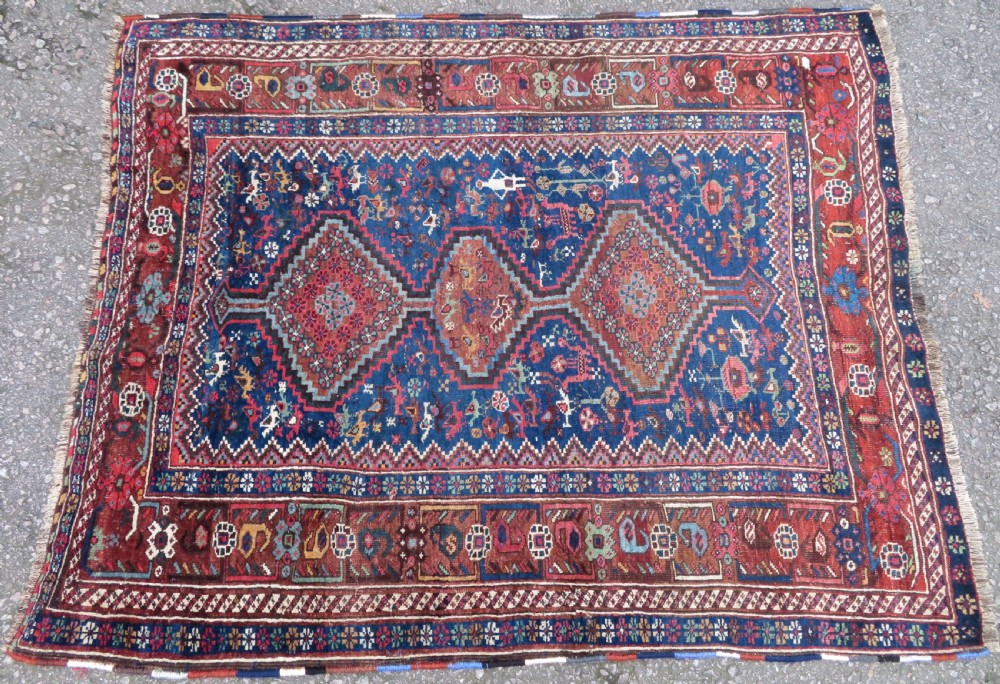 An antique Persian Khamseh rug featuring three central diamond medallions surrounded by small animal motifs and a geometric border in indigo blue and terracotta red tones. View II