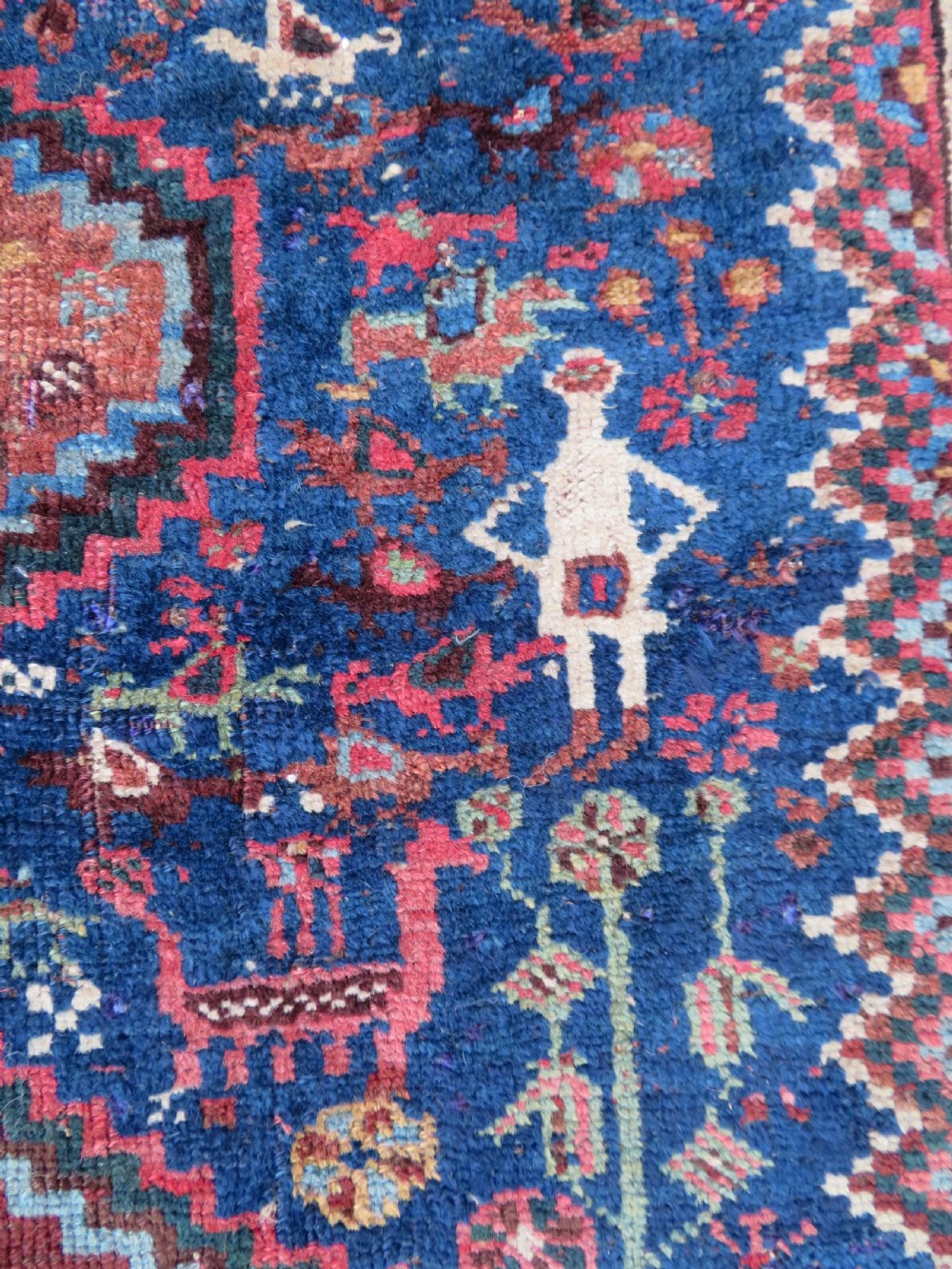 An antique Persian Khamseh rug featuring three central diamond medallions surrounded by small animal motifs and a geometric border in indigo blue and terracotta red tones. View IV