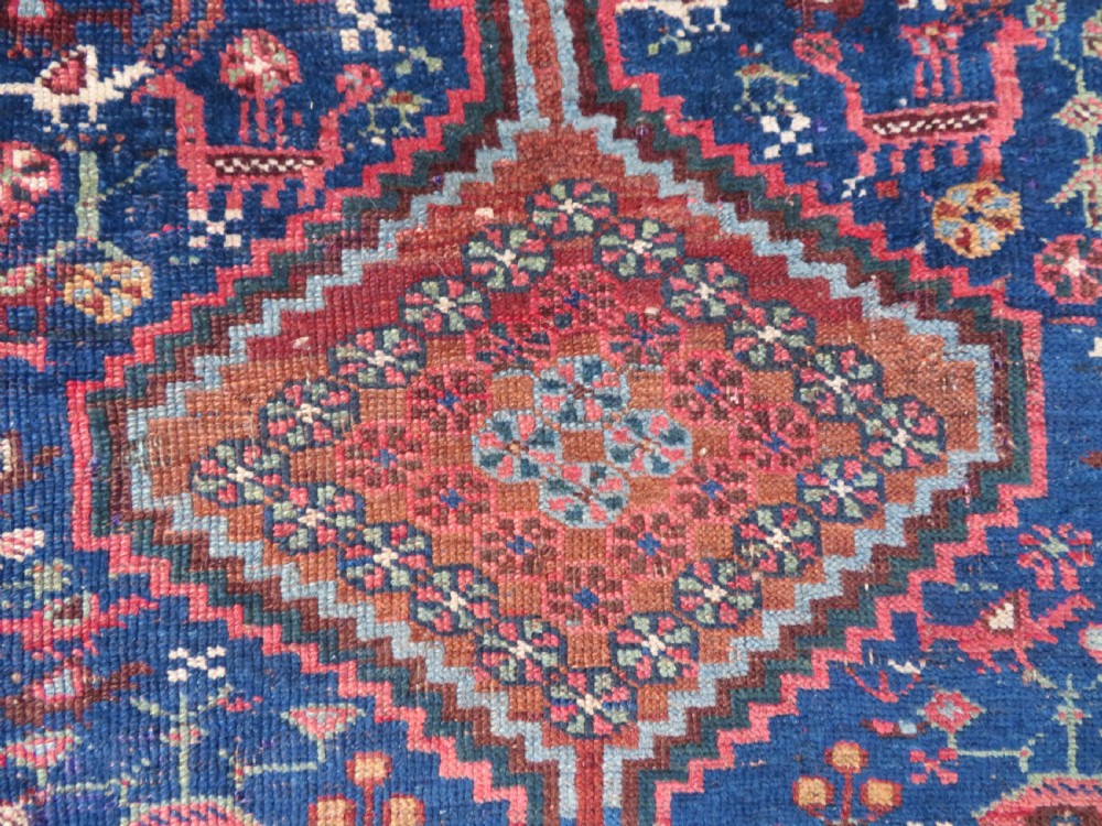 An antique Persian Khamseh rug featuring three central diamond medallions surrounded by small animal motifs and a geometric border in indigo blue and terracotta red tones. View V