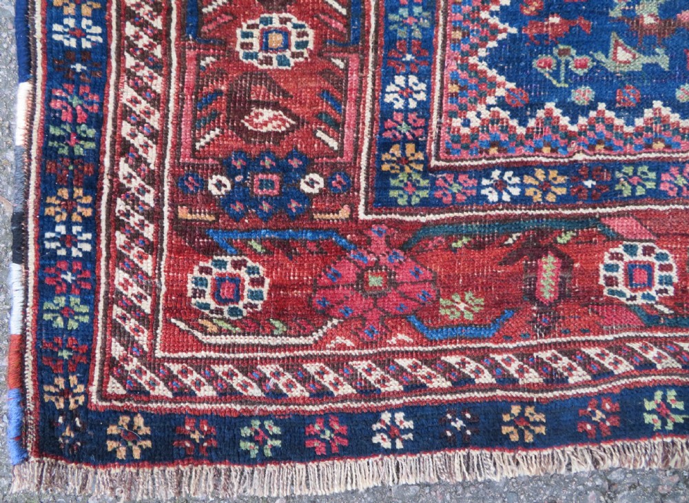 An antique Persian Khamseh rug featuring three central diamond medallions surrounded by small animal motifs and a geometric border in indigo blue and terracotta red tones. View VI