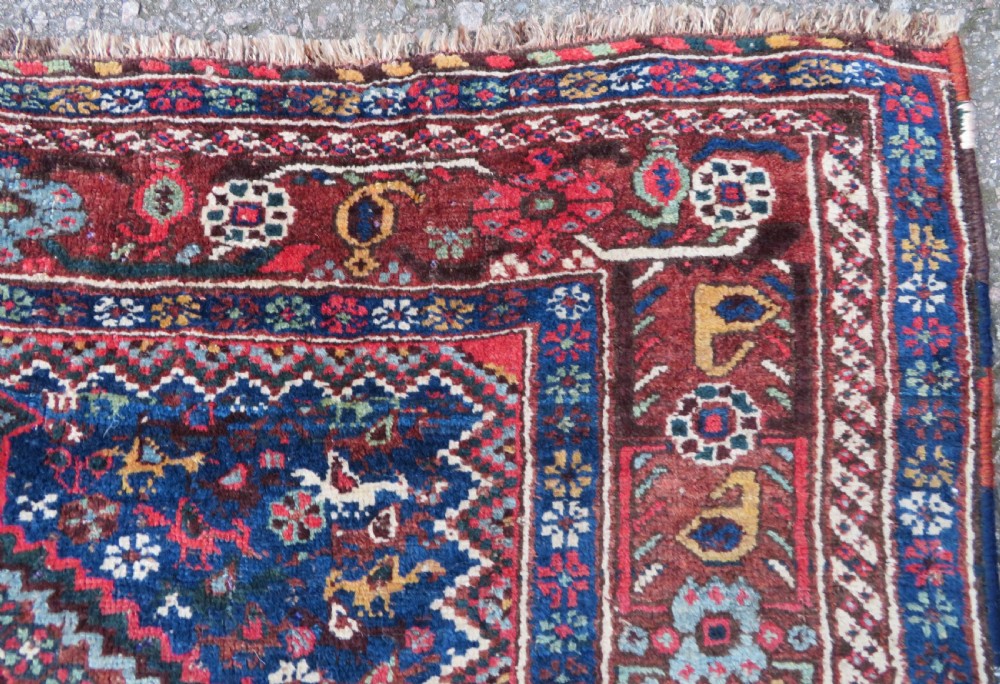 An antique Persian Khamseh rug featuring three central diamond medallions surrounded by small animal motifs and a geometric border in indigo blue and terracotta red tones. View VII