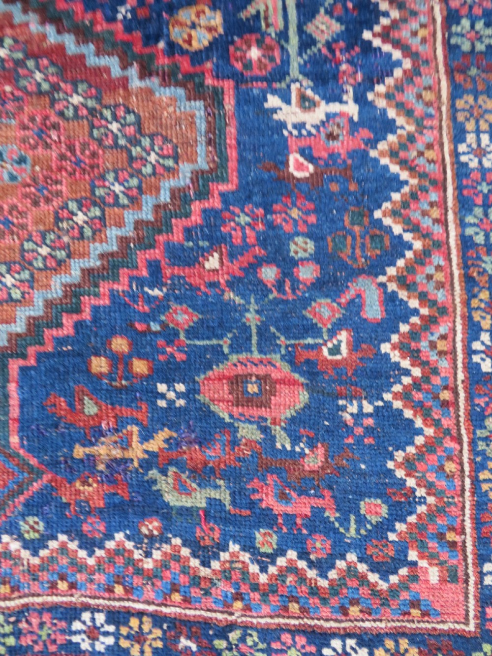 An antique Persian Khamseh rug featuring three central diamond medallions surrounded by small animal motifs and a geometric border in indigo blue and terracotta red tones. View IX