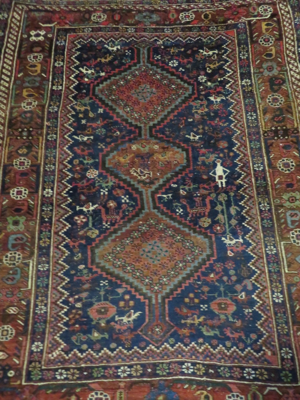 An antique Persian Khamseh rug featuring three central diamond medallions surrounded by small animal motifs and a geometric border in indigo blue and terracotta red tones. View XV
