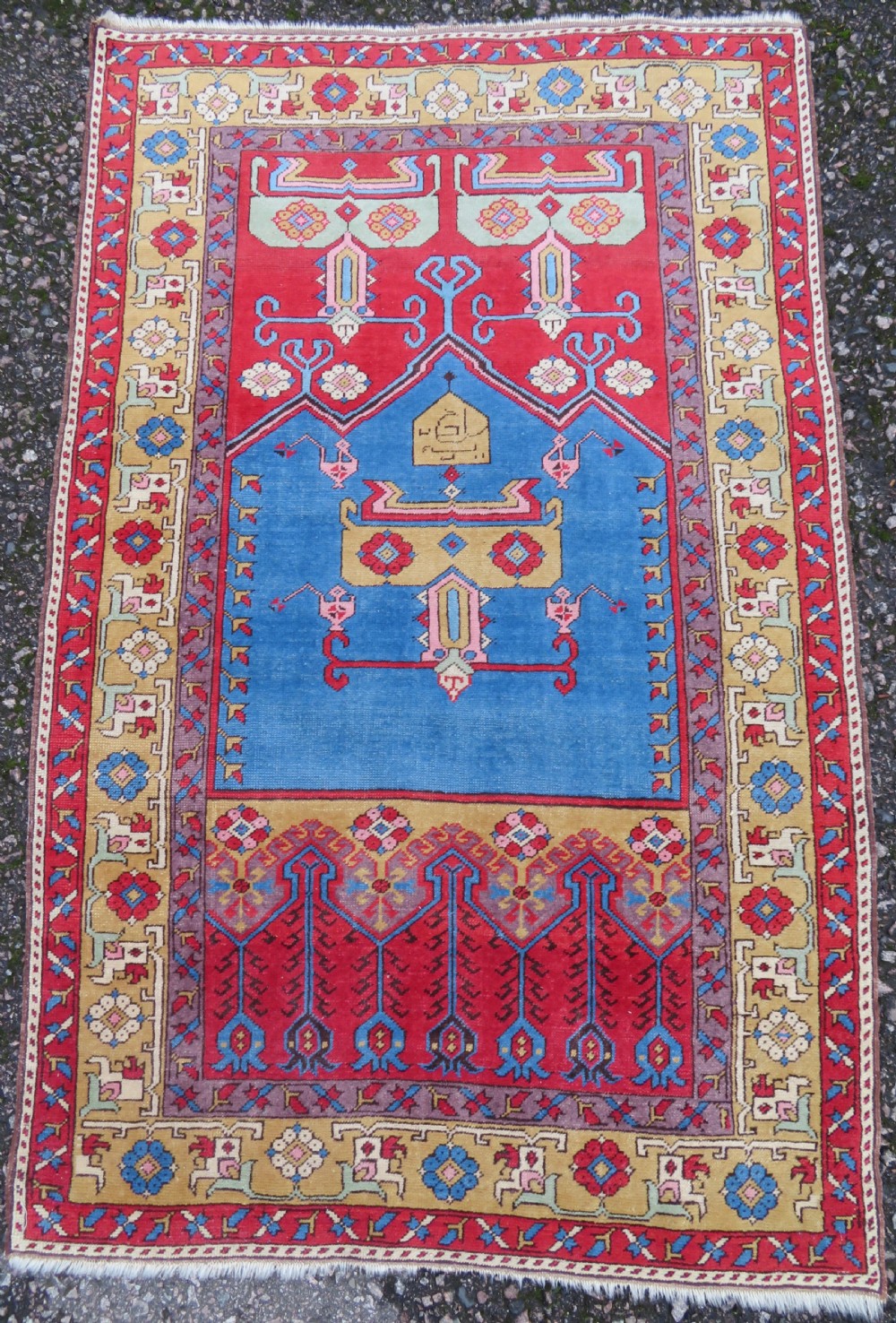 A mid-19th-century hand-knotted Turkish Ladik prayer rug featuring a blue central niche on a red ground with inverted tulip motifs and a patterned yellow border.