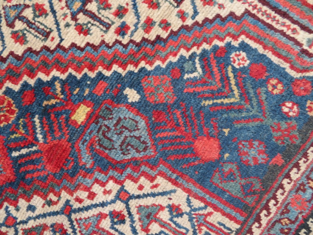 An antique Khamseh Basseri hand-knotted wool rug featuring geometric diamond medallions in red, blue, and ivory tones. View III