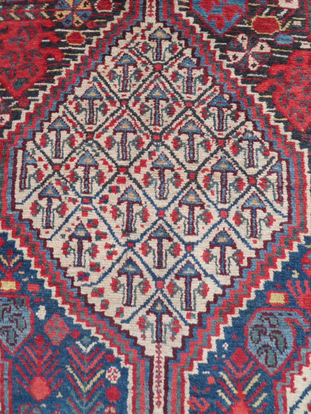 An antique Khamseh Basseri hand-knotted wool rug featuring geometric diamond medallions in red, blue, and ivory tones. View IV