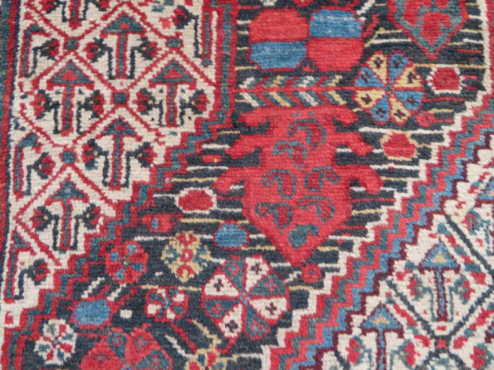 An antique Khamseh Basseri hand-knotted wool rug featuring geometric diamond medallions in red, blue, and ivory tones. View V