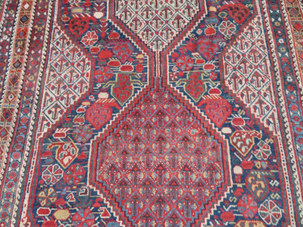 An antique Khamseh Basseri hand-knotted wool rug featuring geometric diamond medallions in red, blue, and ivory tones. View VI