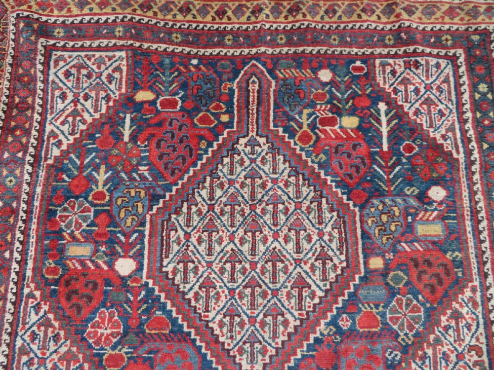 An antique Khamseh Basseri hand-knotted wool rug featuring geometric diamond medallions in red, blue, and ivory tones. View VII
