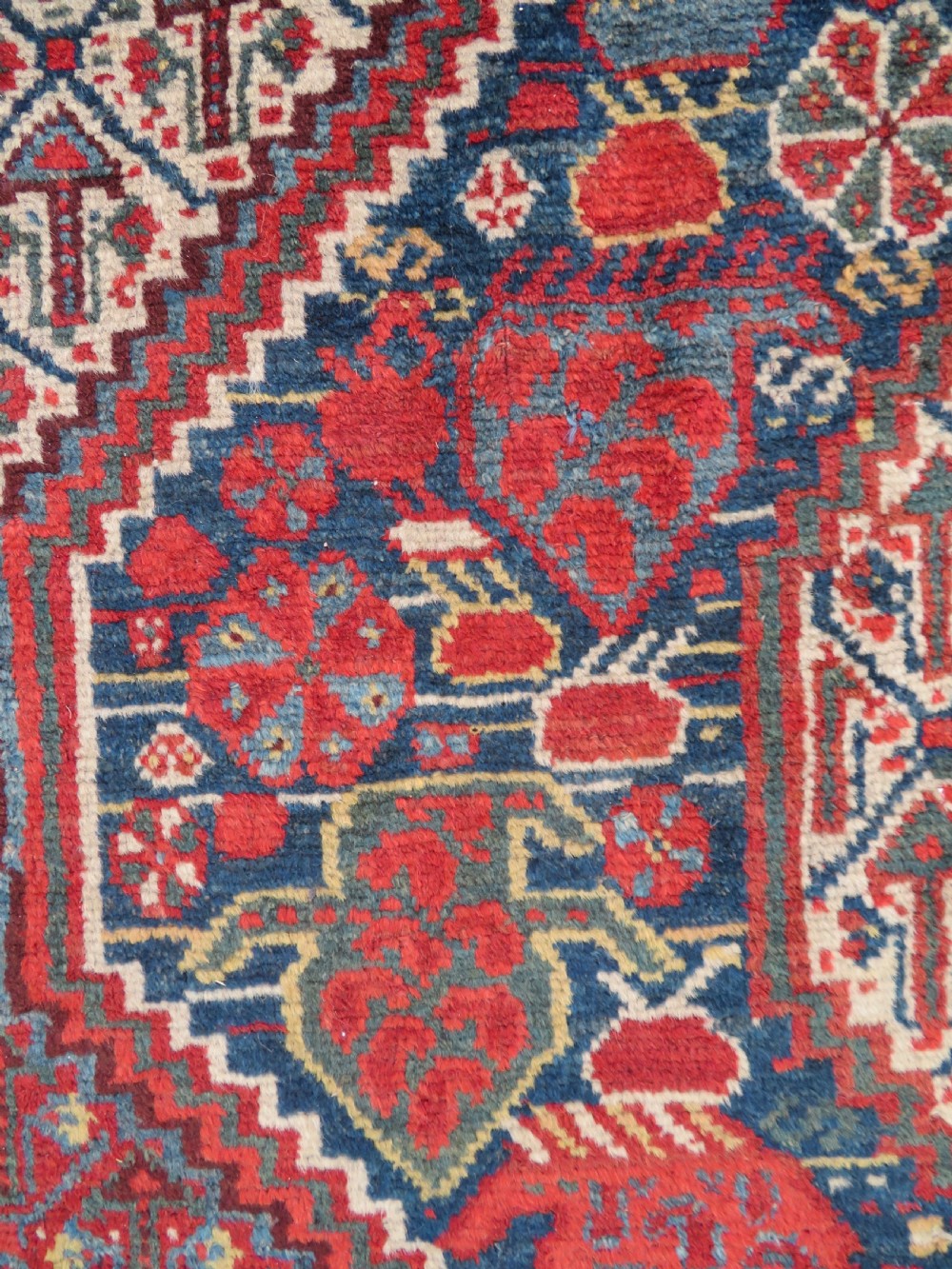 An antique Khamseh Basseri hand-knotted wool rug featuring geometric diamond medallions in red, blue, and ivory tones. View IX