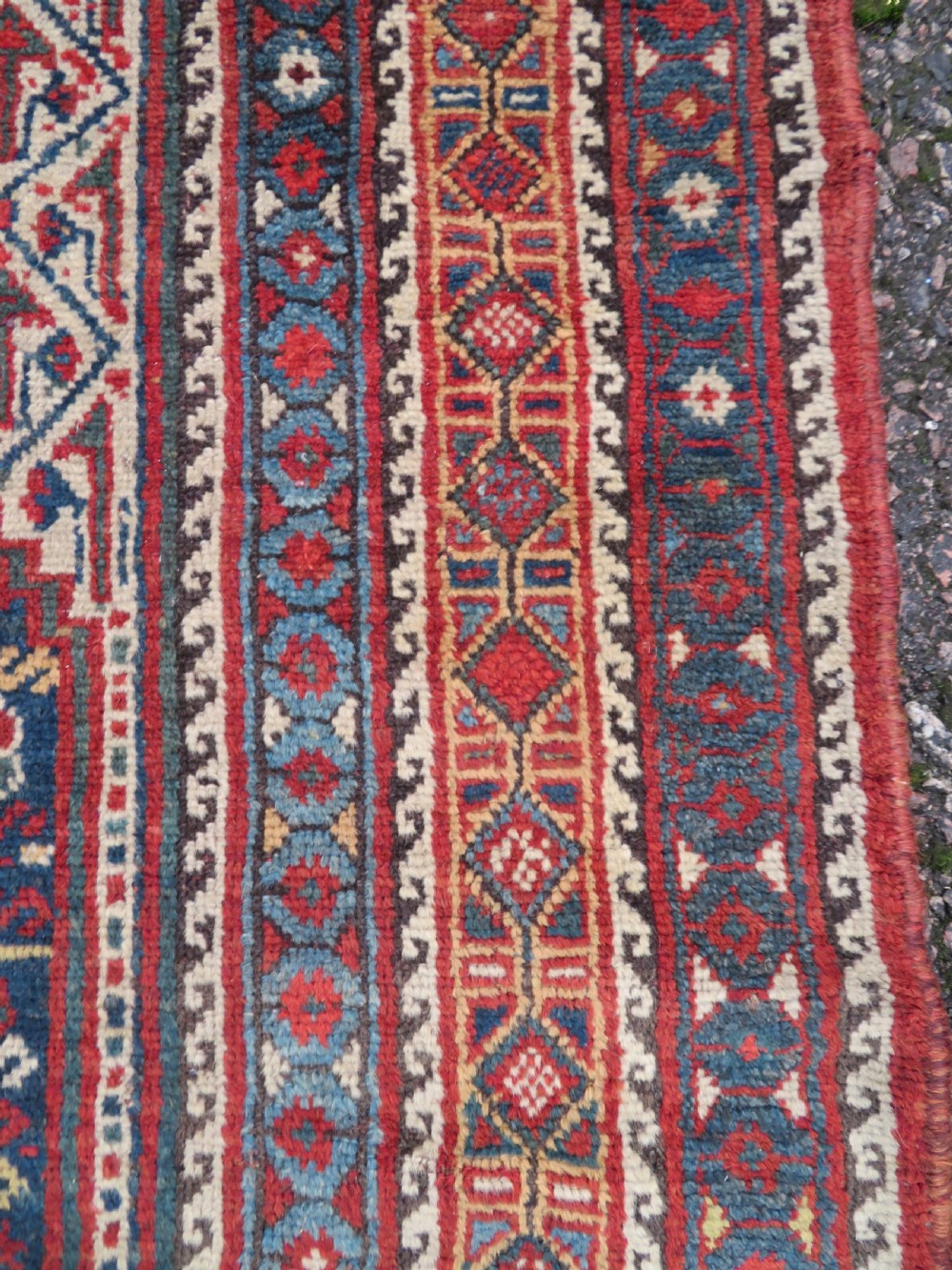 An antique Khamseh Basseri hand-knotted wool rug featuring geometric diamond medallions in red, blue, and ivory tones. View X
