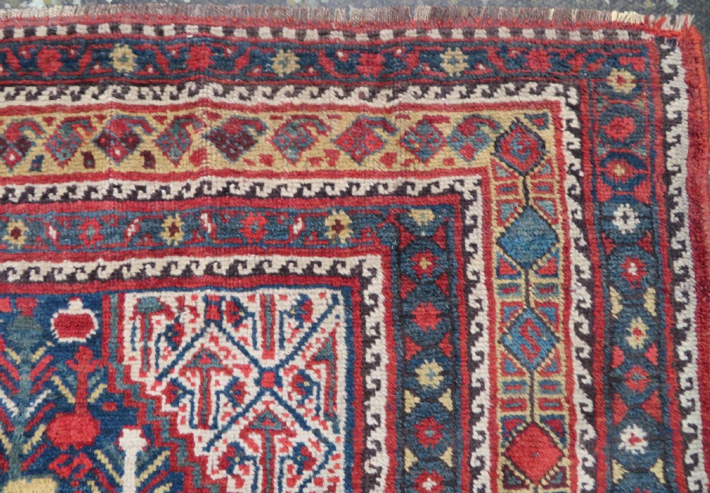 An antique Khamseh Basseri hand-knotted wool rug featuring geometric diamond medallions in red, blue, and ivory tones. View XI