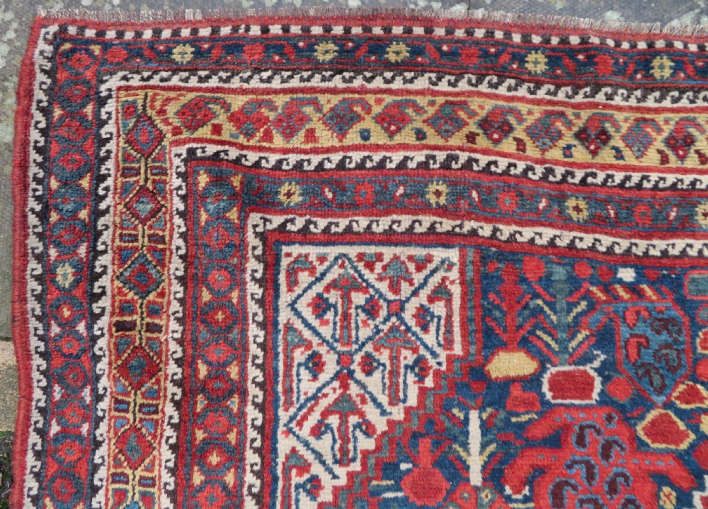 An antique Khamseh Basseri hand-knotted wool rug featuring geometric diamond medallions in red, blue, and ivory tones. View XII