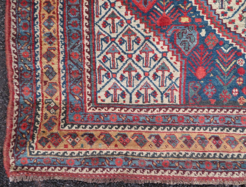 An antique Khamseh Basseri hand-knotted wool rug featuring geometric diamond medallions in red, blue, and ivory tones. View XIII