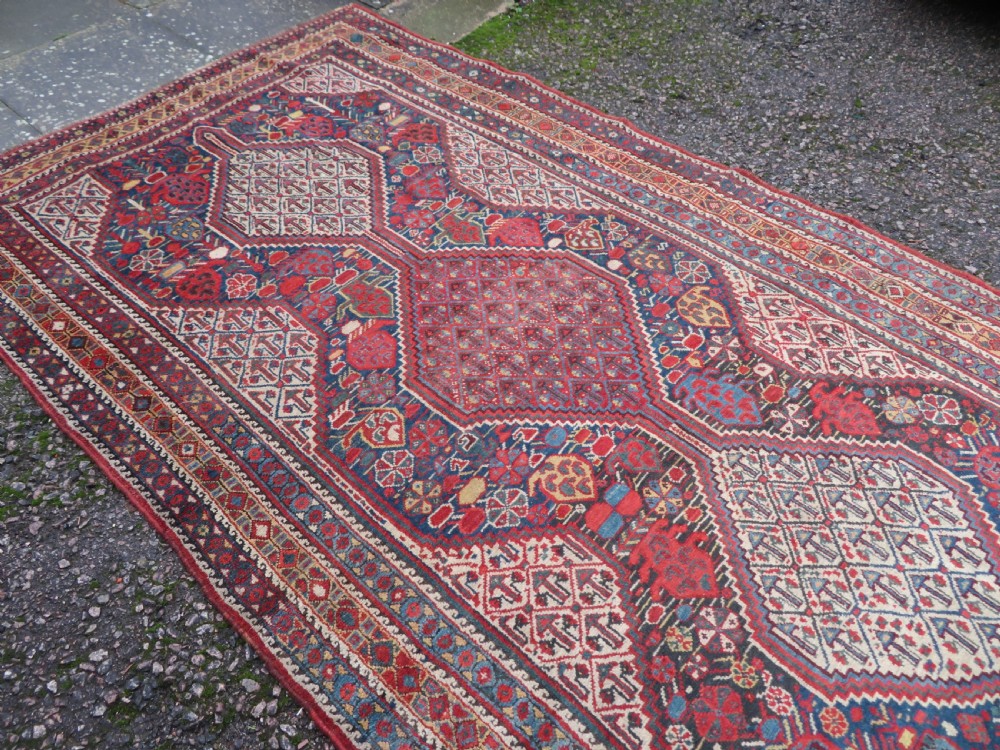 An antique Khamseh Basseri hand-knotted wool rug featuring geometric diamond medallions in red, blue, and ivory tones. View XV