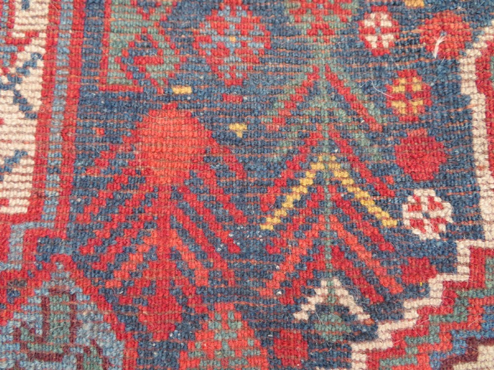 An antique Khamseh Basseri hand-knotted wool rug featuring geometric diamond medallions in red, blue, and ivory tones. View XVII