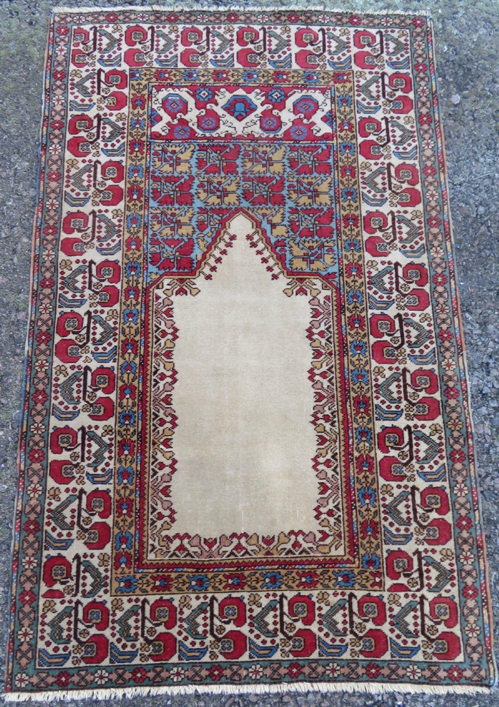 An antique hand-knotted West Anatolian prayer rug featuring a cream central mihrab arch surrounded by geometric borders in red, blue, and yellow.