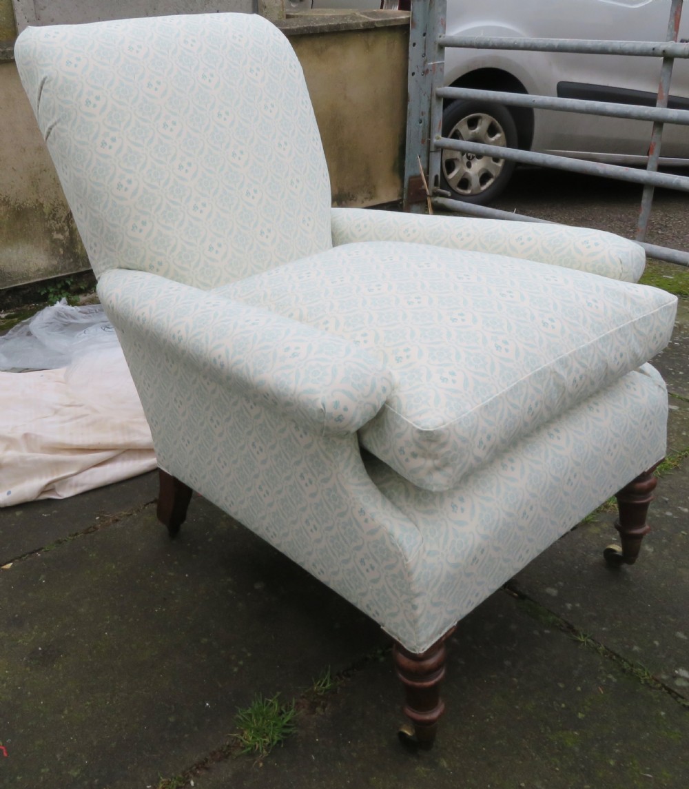 A low-seated Victorian easy chair upholstered in pale blue and cream patterned fabric with turned wooden front legs and brass castors.