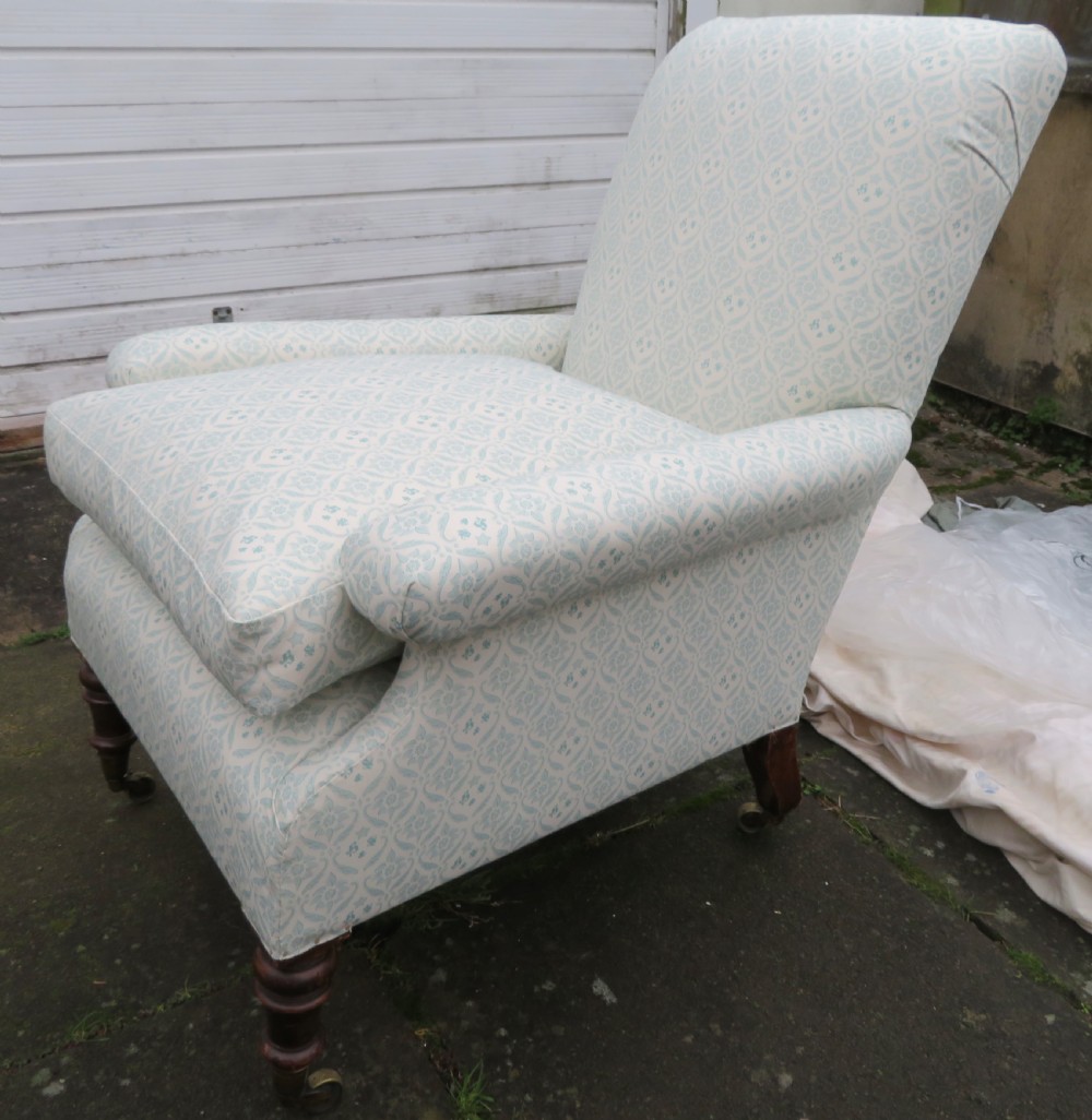 A low-seated Victorian easy chair upholstered in pale blue and cream patterned fabric with turned wooden front legs and brass castors. View II