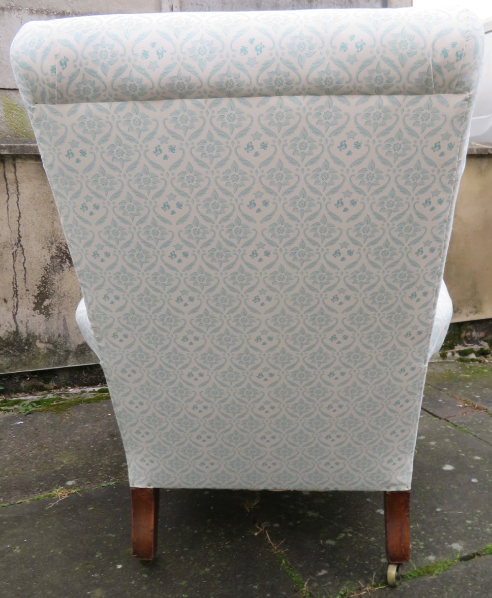 A low-seated Victorian easy chair upholstered in pale blue and cream patterned fabric with turned wooden front legs and brass castors. View III