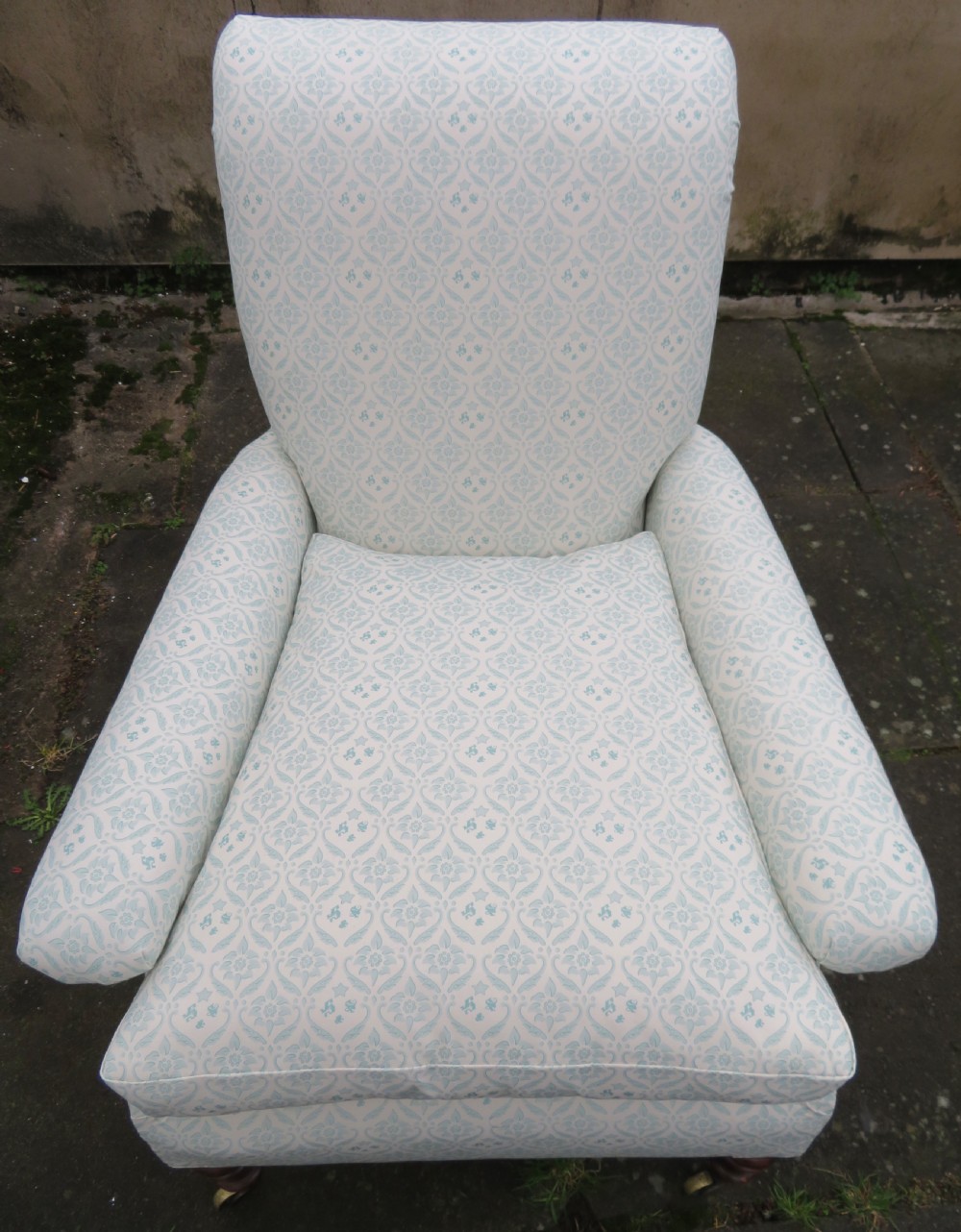 A low-seated Victorian easy chair upholstered in pale blue and cream patterned fabric with turned wooden front legs and brass castors. View VII