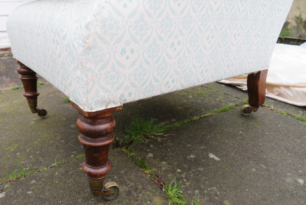 A low-seated Victorian easy chair upholstered in pale blue and cream patterned fabric with turned wooden front legs and brass castors. View X