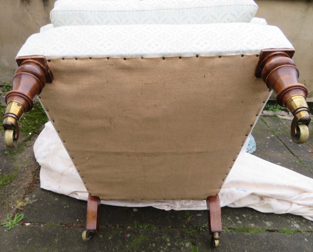 A low-seated Victorian easy chair upholstered in pale blue and cream patterned fabric with turned wooden front legs and brass castors. View XI