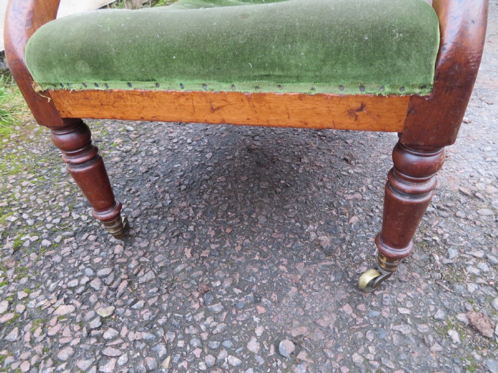 A Victorian mahogany elbow armchair upholstered in button-backed green velvet with scrolled arms and brass castors. View VIII