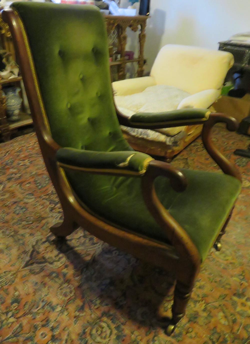A Victorian mahogany elbow armchair upholstered in button-backed green velvet with scrolled arms and brass castors. View XXI