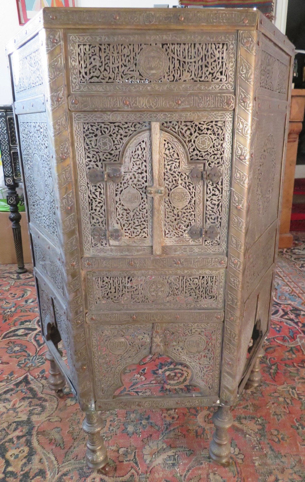 An octagonal Cairo ware brass kursi table with silver and copper inlay, Arabic calligraphy, pierced fretwork panels, and small cupboard doors on turned legs.