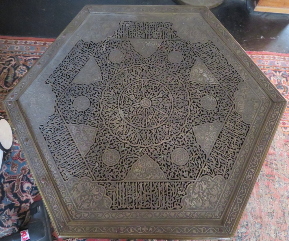 An octagonal Cairo ware brass kursi table with silver and copper inlay, Arabic calligraphy, pierced fretwork panels, and small cupboard doors on turned legs. View II