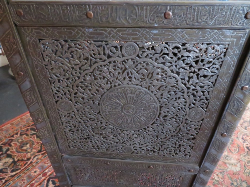 An octagonal Cairo ware brass kursi table with silver and copper inlay, Arabic calligraphy, pierced fretwork panels, and small cupboard doors on turned legs. View III