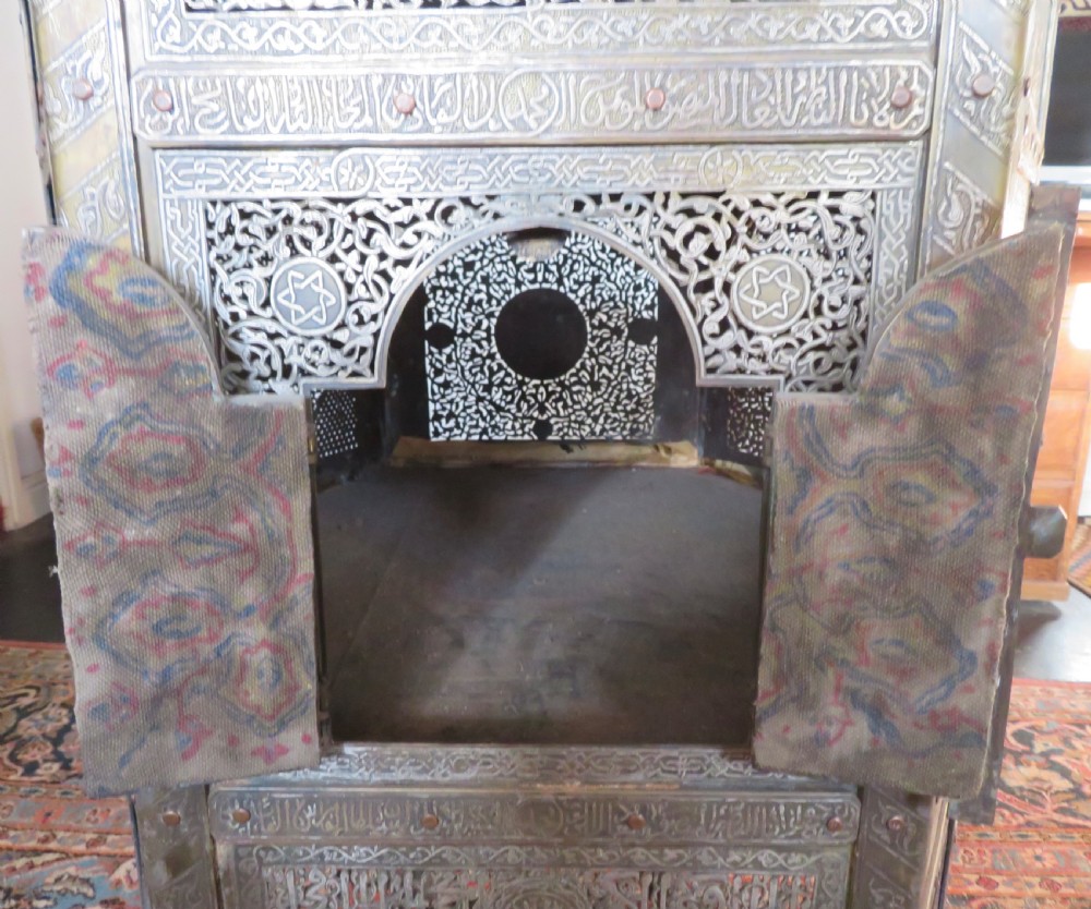 An octagonal Cairo ware brass kursi table with silver and copper inlay, Arabic calligraphy, pierced fretwork panels, and small cupboard doors on turned legs. View VI