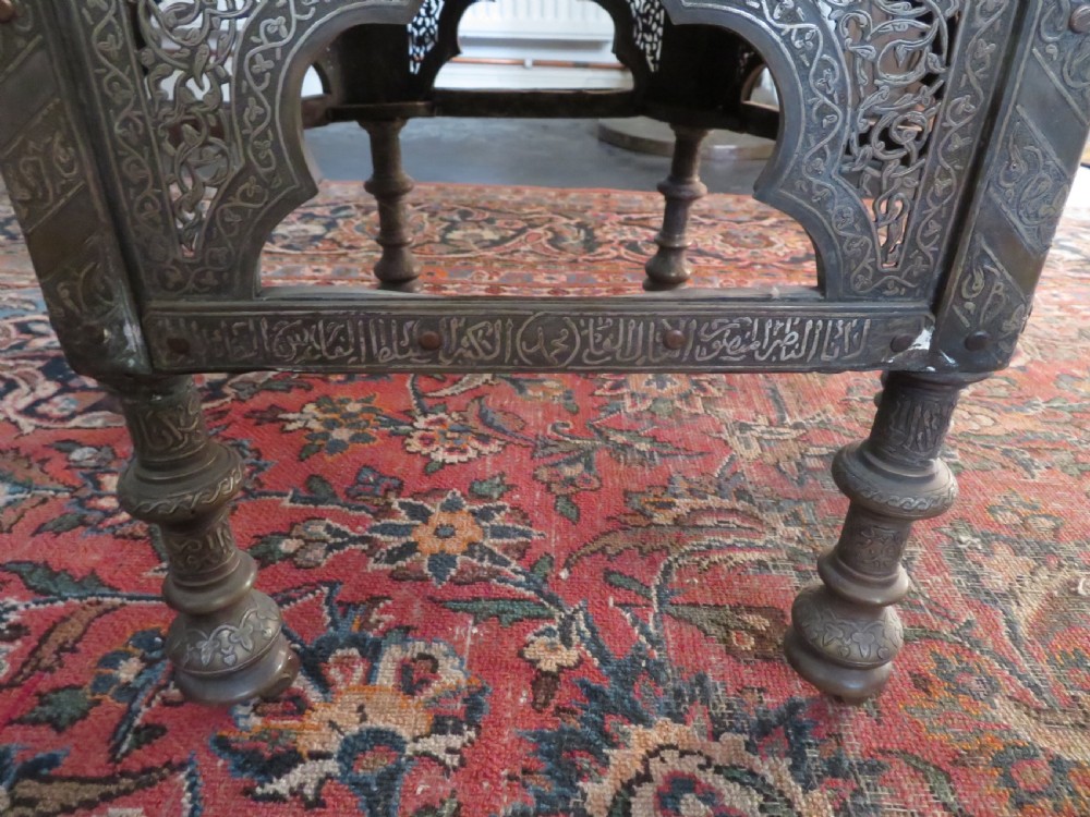 An octagonal Cairo ware brass kursi table with silver and copper inlay, Arabic calligraphy, pierced fretwork panels, and small cupboard doors on turned legs. View VIII