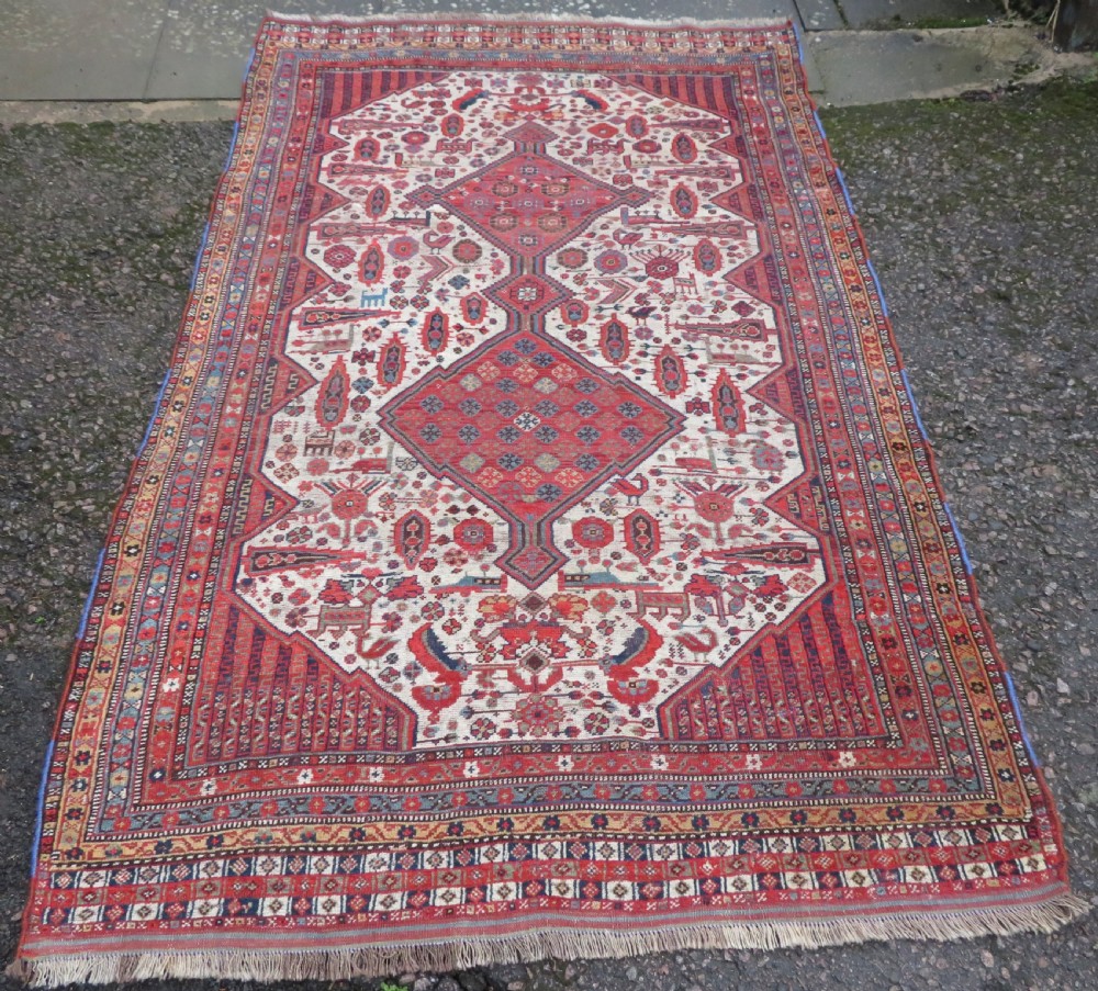 An antique hand-knotted Khamseh tribal rug featuring two diamond medallions on an ivory field filled with bird and geometric motifs, surrounded by a red patterned border.