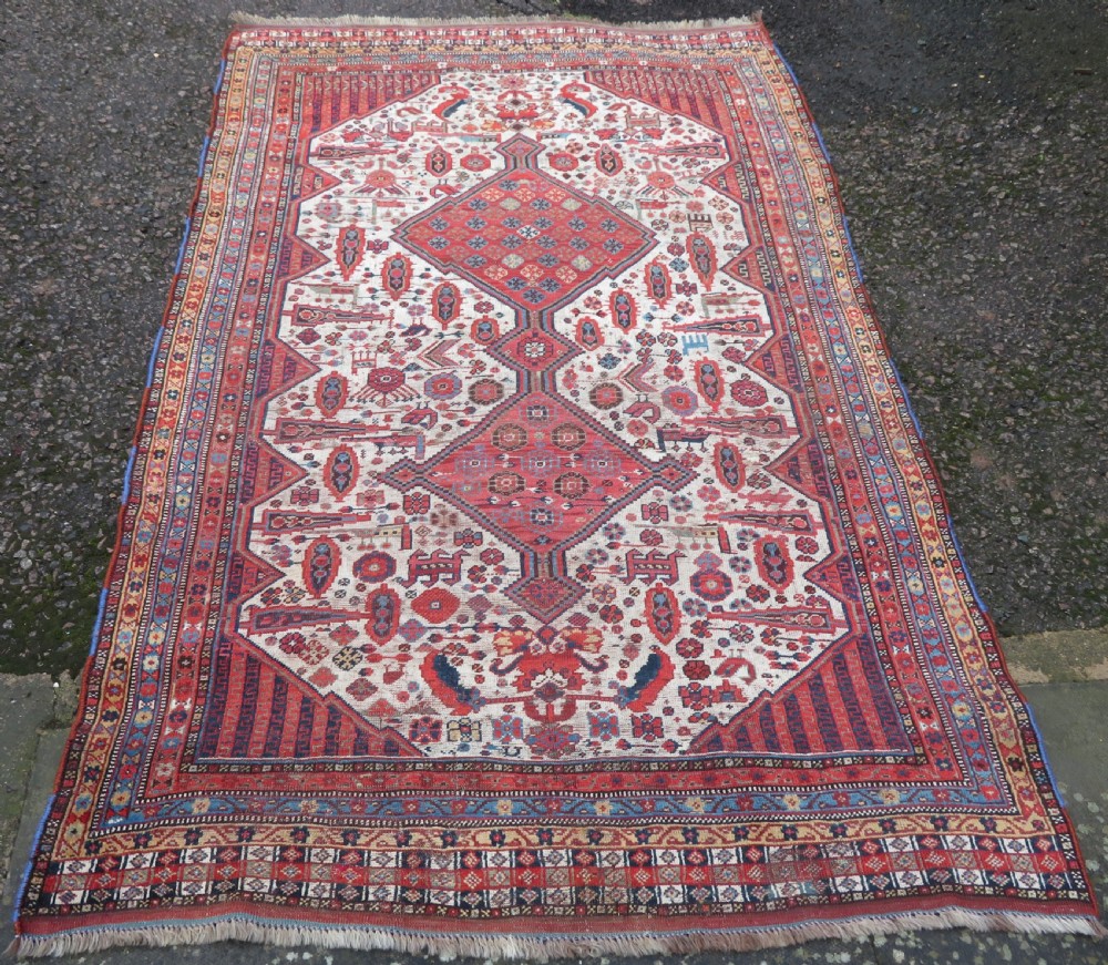 An antique hand-knotted Khamseh tribal rug featuring two diamond medallions on an ivory field filled with bird and geometric motifs, surrounded by a red patterned border. View II