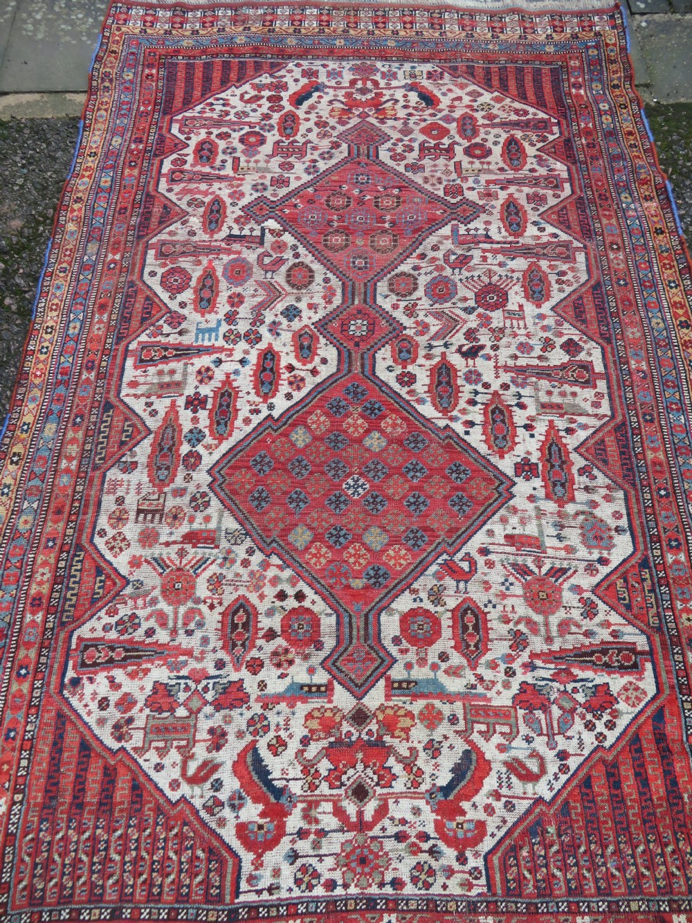 An antique hand-knotted Khamseh tribal rug featuring two diamond medallions on an ivory field filled with bird and geometric motifs, surrounded by a red patterned border. View III