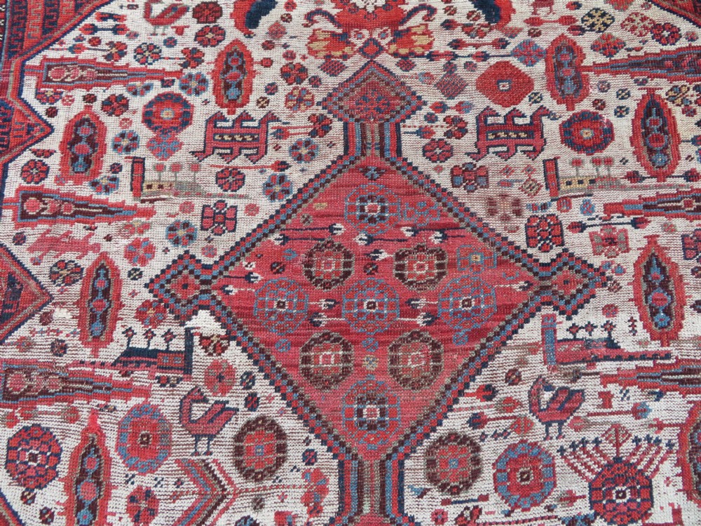 An antique hand-knotted Khamseh tribal rug featuring two diamond medallions on an ivory field filled with bird and geometric motifs, surrounded by a red patterned border. View IV