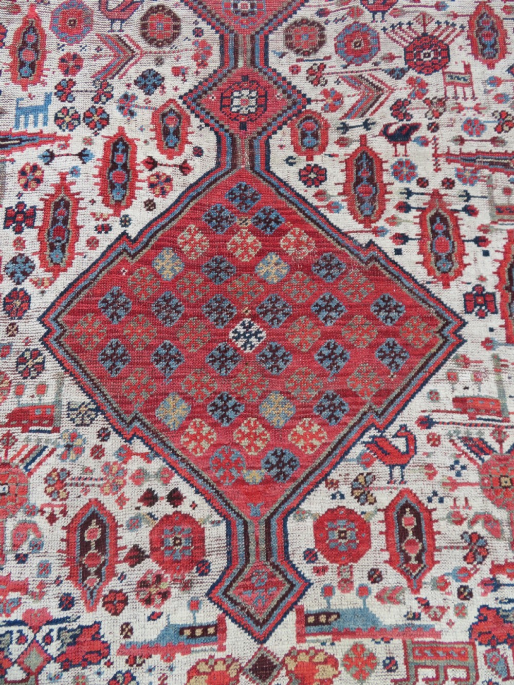 An antique hand-knotted Khamseh tribal rug featuring two diamond medallions on an ivory field filled with bird and geometric motifs, surrounded by a red patterned border. View VI