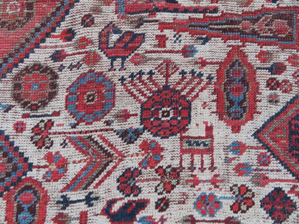 An antique hand-knotted Khamseh tribal rug featuring two diamond medallions on an ivory field filled with bird and geometric motifs, surrounded by a red patterned border. View VII