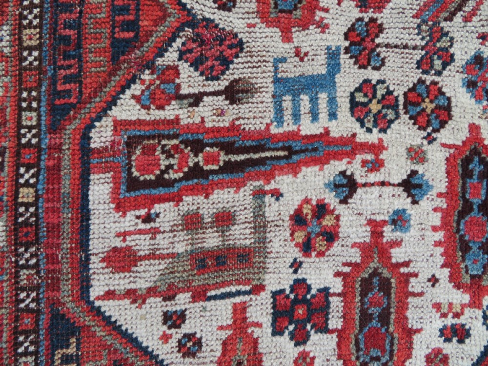 An antique hand-knotted Khamseh tribal rug featuring two diamond medallions on an ivory field filled with bird and geometric motifs, surrounded by a red patterned border. View X