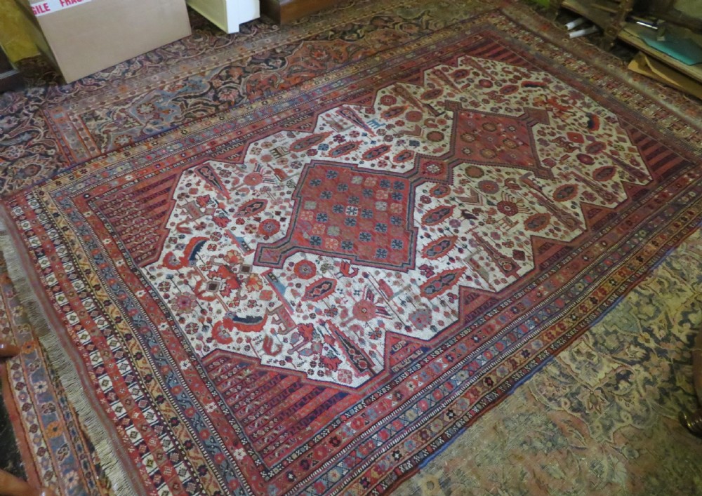 An antique hand-knotted Khamseh tribal rug featuring two diamond medallions on an ivory field filled with bird and geometric motifs, surrounded by a red patterned border. View XXI