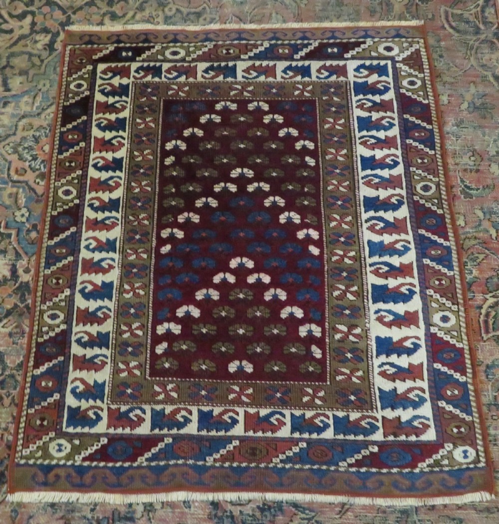 A small antique Turkish Bergama wool rug featuring a deep red central field with repeating floral-like motifs surrounded by geometric cream and blue borders. View II