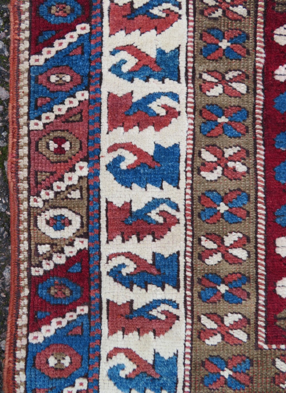 A small antique Turkish Bergama wool rug featuring a deep red central field with repeating floral-like motifs surrounded by geometric cream and blue borders. View IV