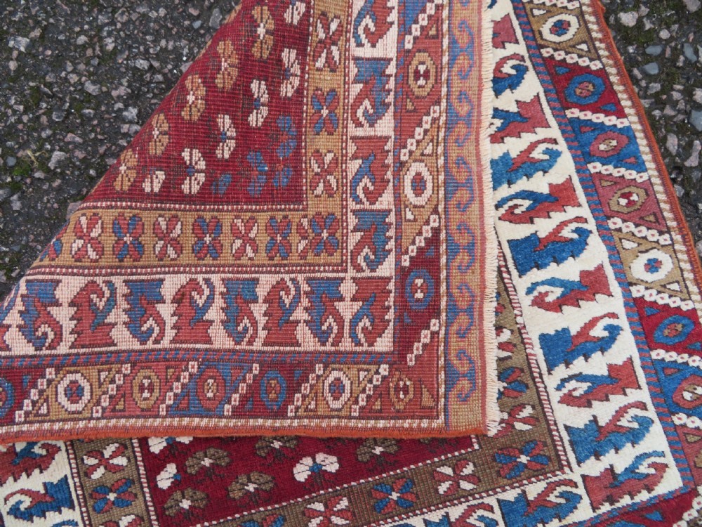 A small antique Turkish Bergama wool rug featuring a deep red central field with repeating floral-like motifs surrounded by geometric cream and blue borders. View VI