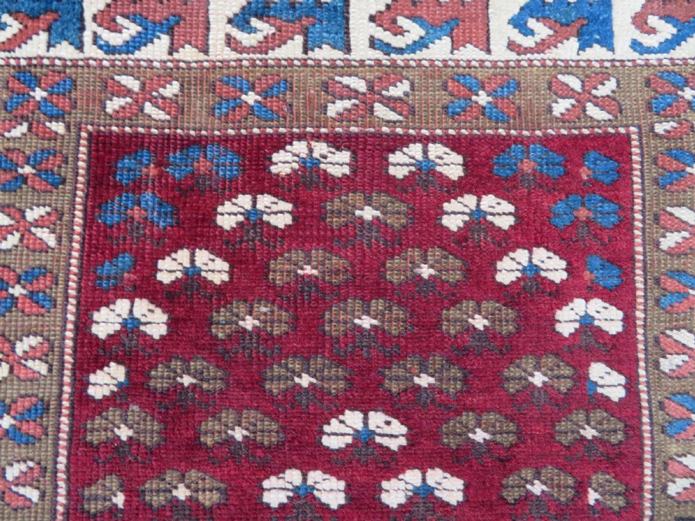 A small antique Turkish Bergama wool rug featuring a deep red central field with repeating floral-like motifs surrounded by geometric cream and blue borders. View VII