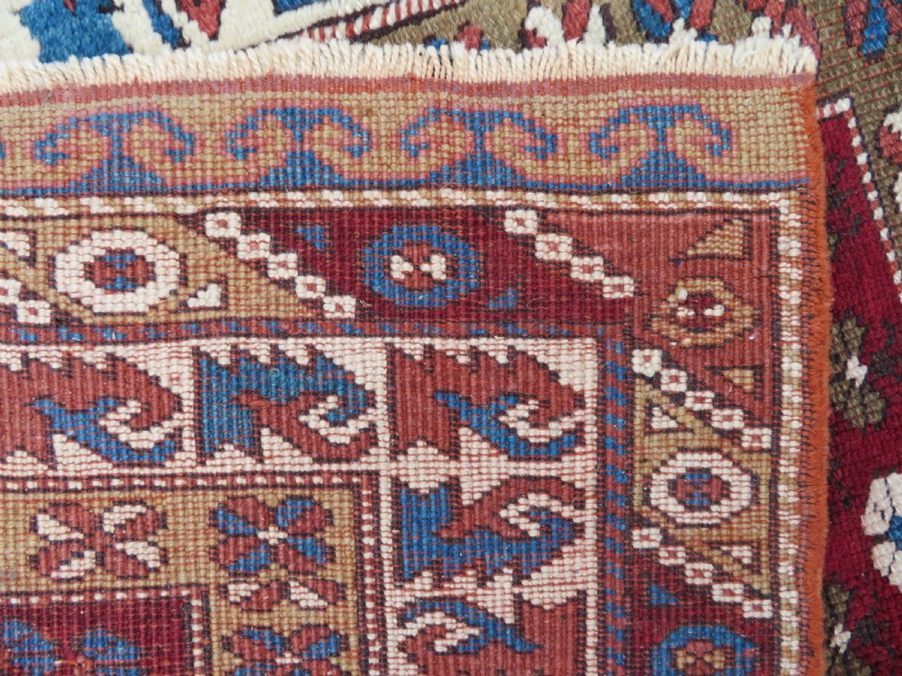 A small antique Turkish Bergama wool rug featuring a deep red central field with repeating floral-like motifs surrounded by geometric cream and blue borders. View VIII